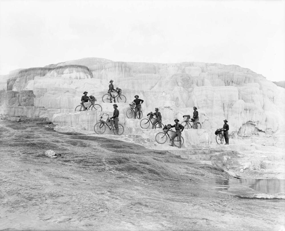 Group of nine cyclists with bikes on a rocky, terraced landscape.