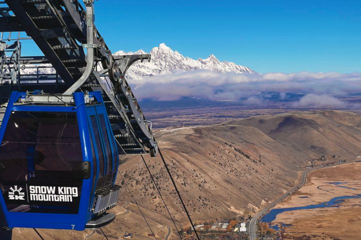 Blue gondola at Snow King Mountain overlooking a valley and snowy peaks.