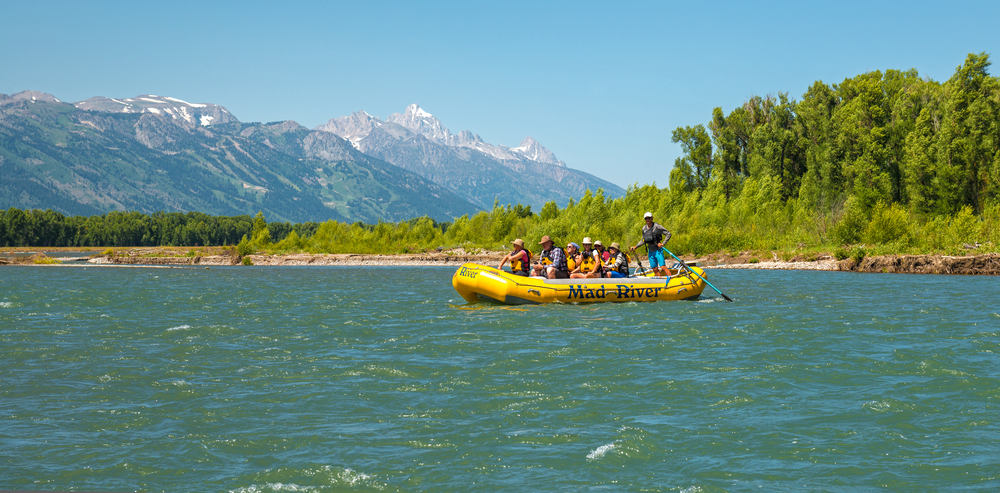 Group rafting on a river with mountains in the background on a sunny day.