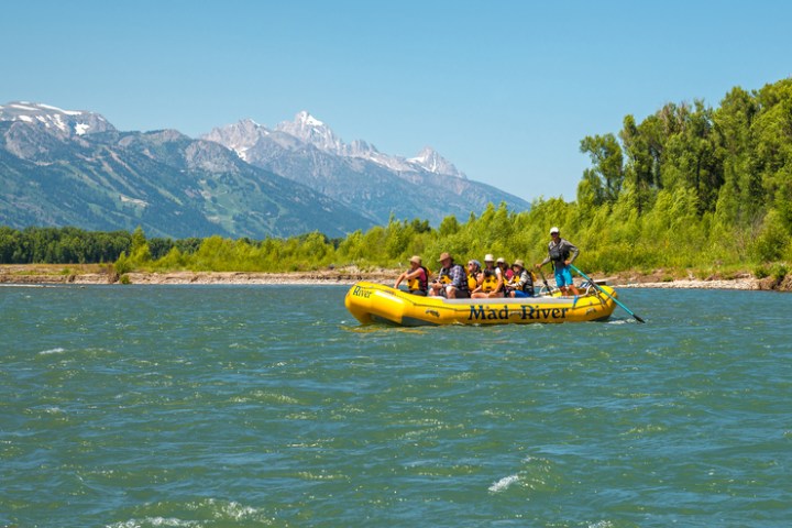 A group rafting in a yellow boat on a river with mountains and trees in the background.