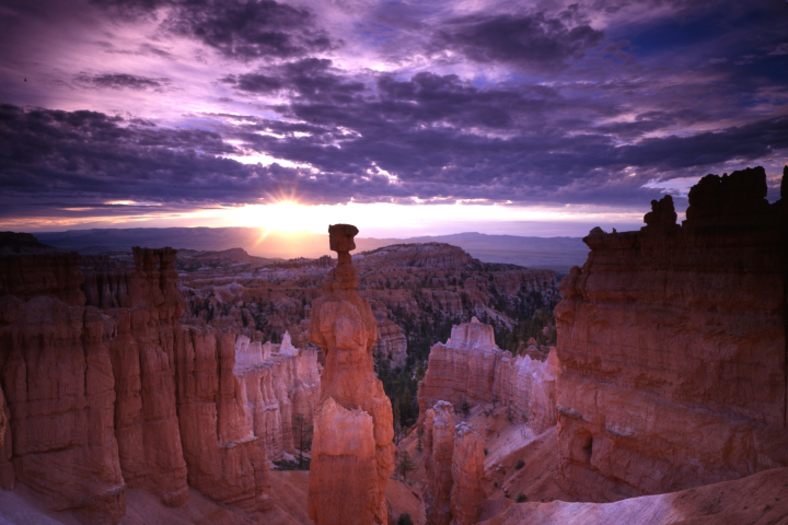 Sunrise over rock formations in Bryce Canyon with a dramatic purple sky.