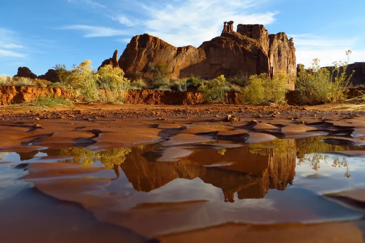 Rocky desert landscape with water reflections under a clear blue sky.