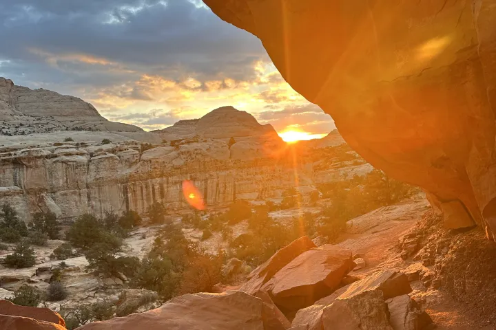 Sunset over rocky canyon landscape with sunlight streaming through arch.