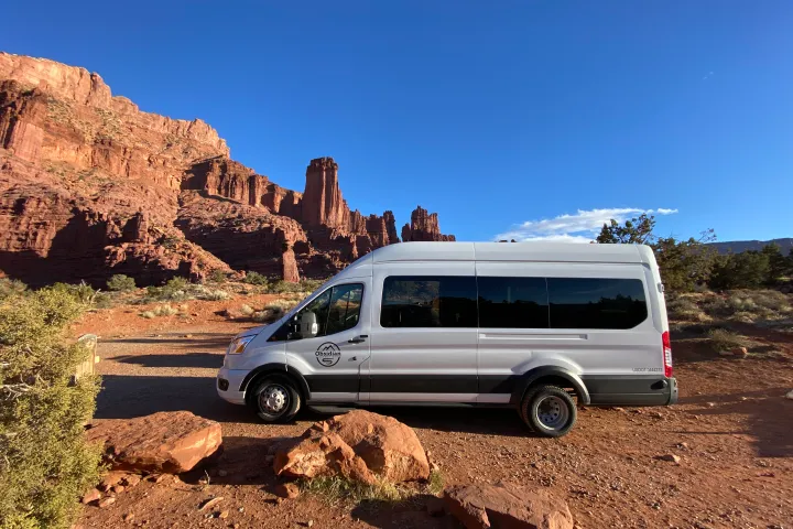 White van parked in desert landscape with red rock formations under a clear blue sky.