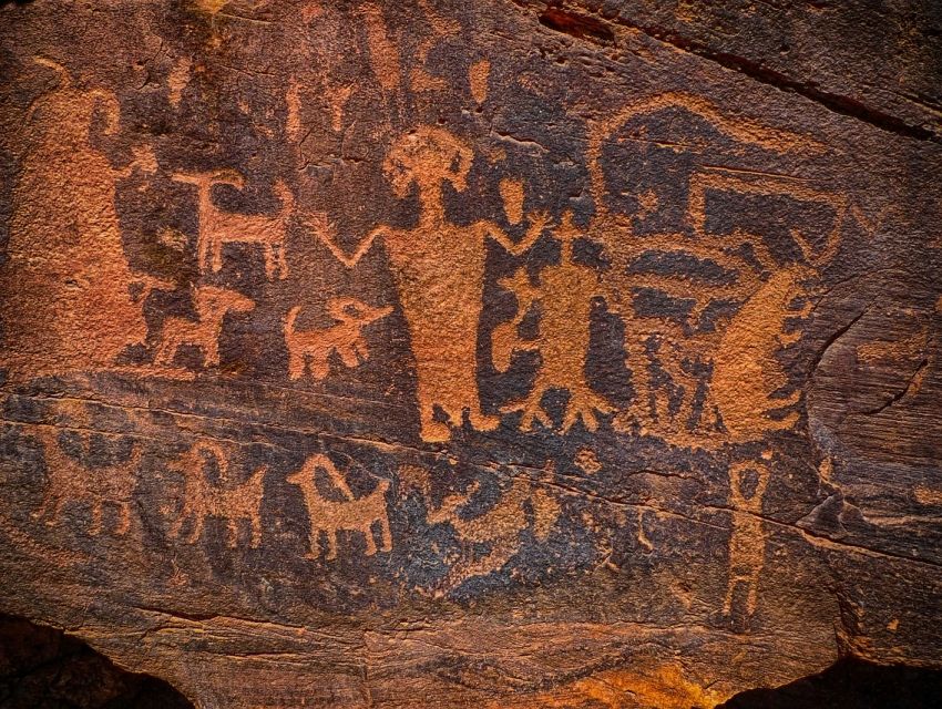 Ancient petroglyphs on rock showing human and animal figures with intricate patterns.