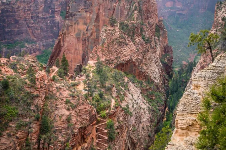 Steep zigzag trail leading up a rocky peak in a canyon with scattered trees.