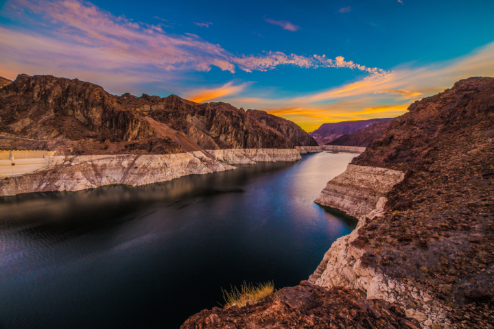 River flowing through rocky canyon at sunset, vibrant sky with clouds.