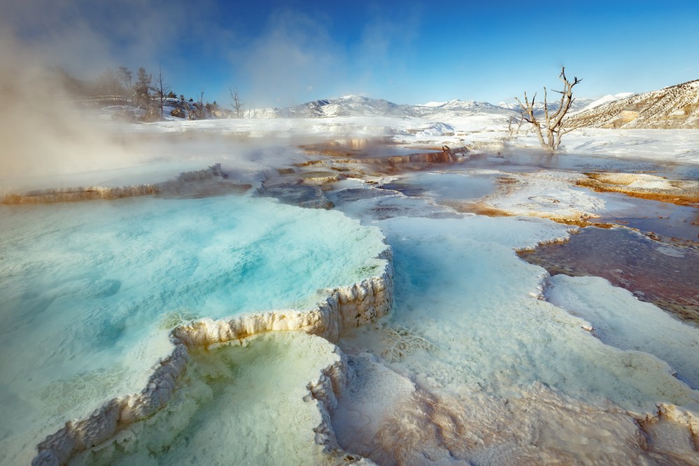 Colorful geothermal hot springs with steam under a clear blue sky.