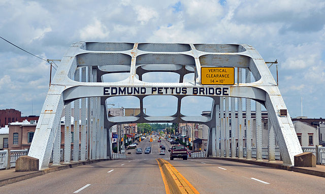 View of Edmund Pettus Bridge from roadway, city skyline in background.