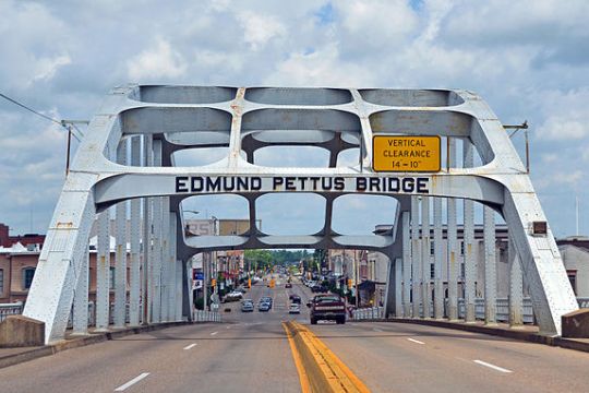 View of Edmund Pettus Bridge from roadway, city skyline in background.