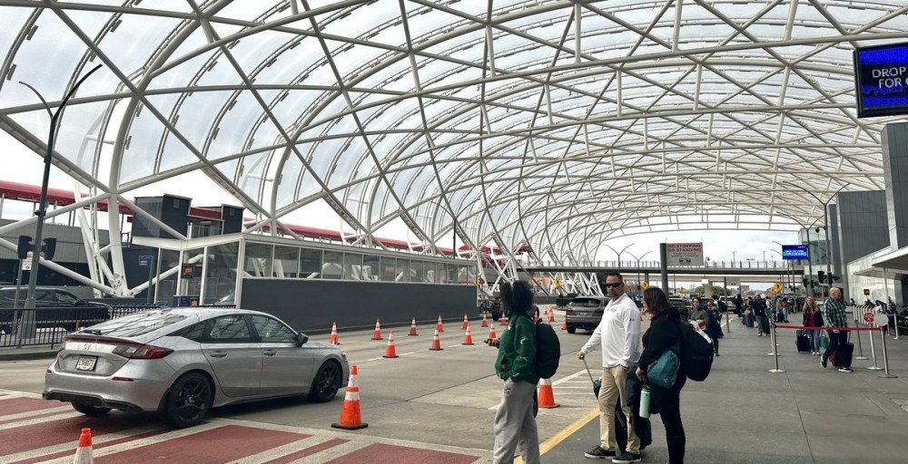 People and cars at the Atlanta-Hartsfield airport drop-off area under an arched canopy.