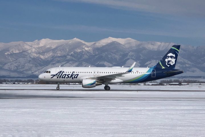 Airplane on snowy runway with mountains in the background.