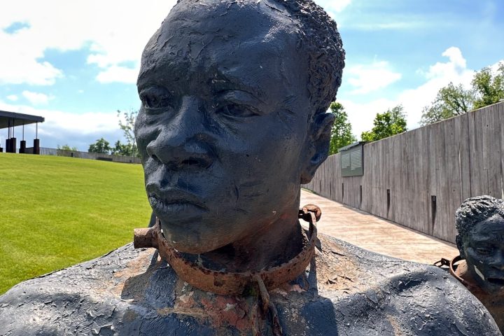 Close-up of a weathered statue of a person with chains, set outdoors under a blue sky.