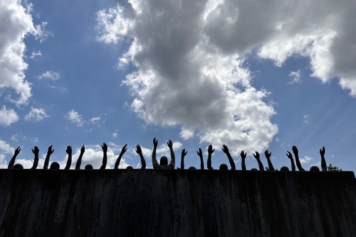 Silhouetted arms raised against a cloudy sky above a dark wall.