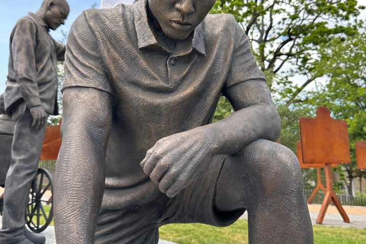 Bronze sculpture of a kneeling young man with a pensive expression.