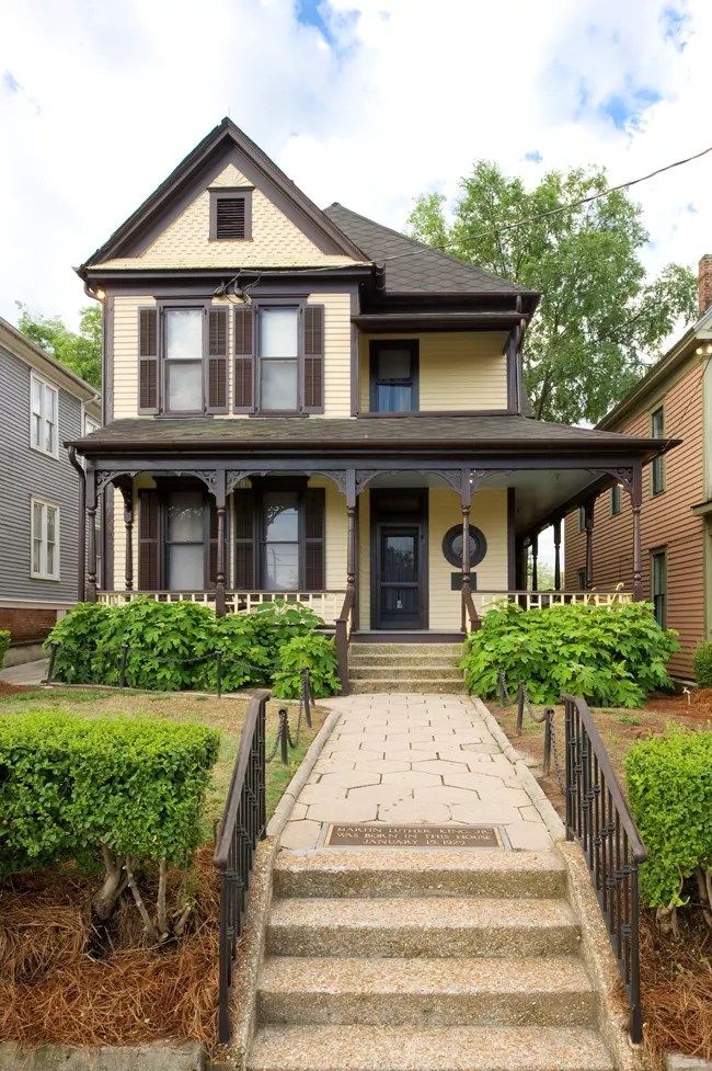 Yellow Victorian house with brown shutters, front porch, and walkway.