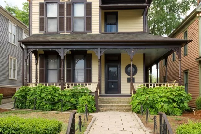 Yellow Victorian house with brown shutters, front porch, and walkway.