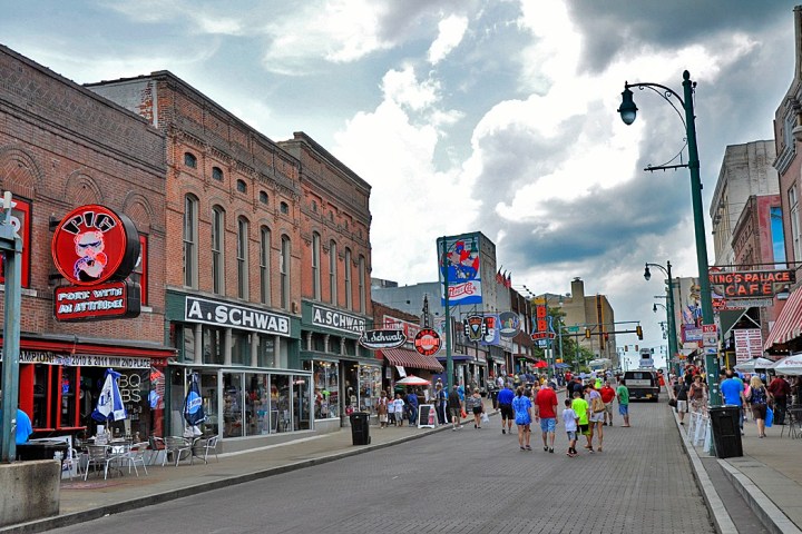 Busy street scene with shops and neon signs, cloudy sky above.