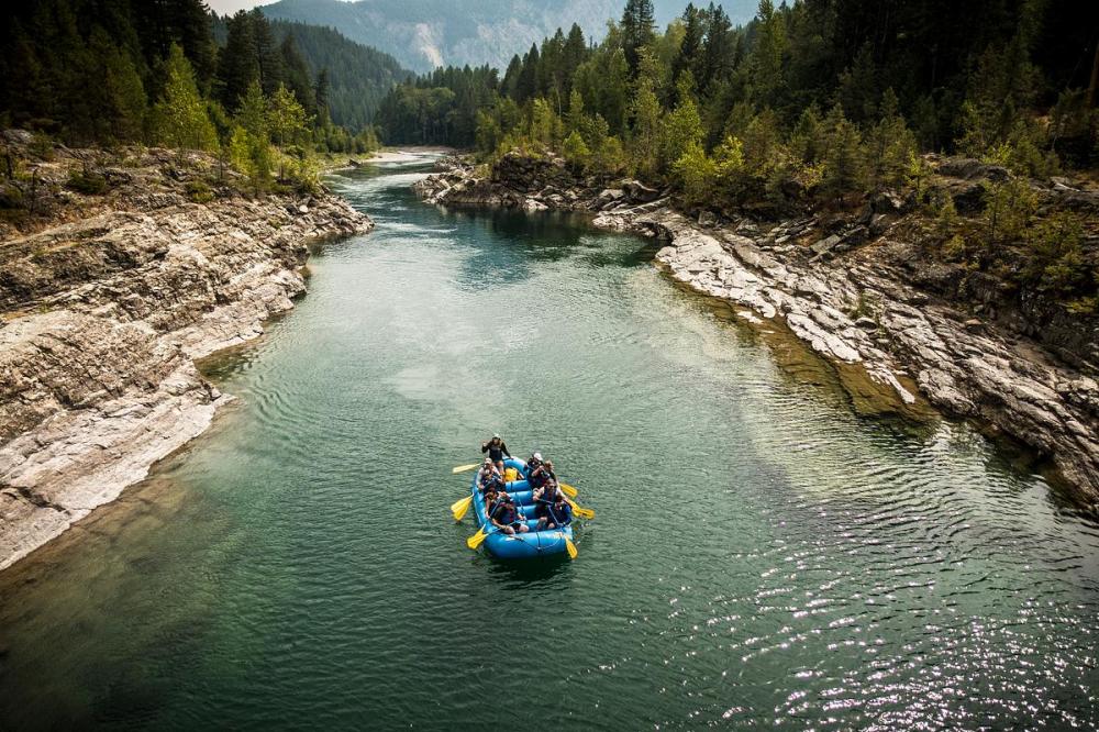 Group rafting on a narrow river surrounded by rocky banks and trees.