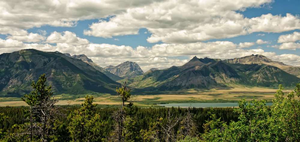 Mountain range with trees in foreground under a partly cloudy sky.