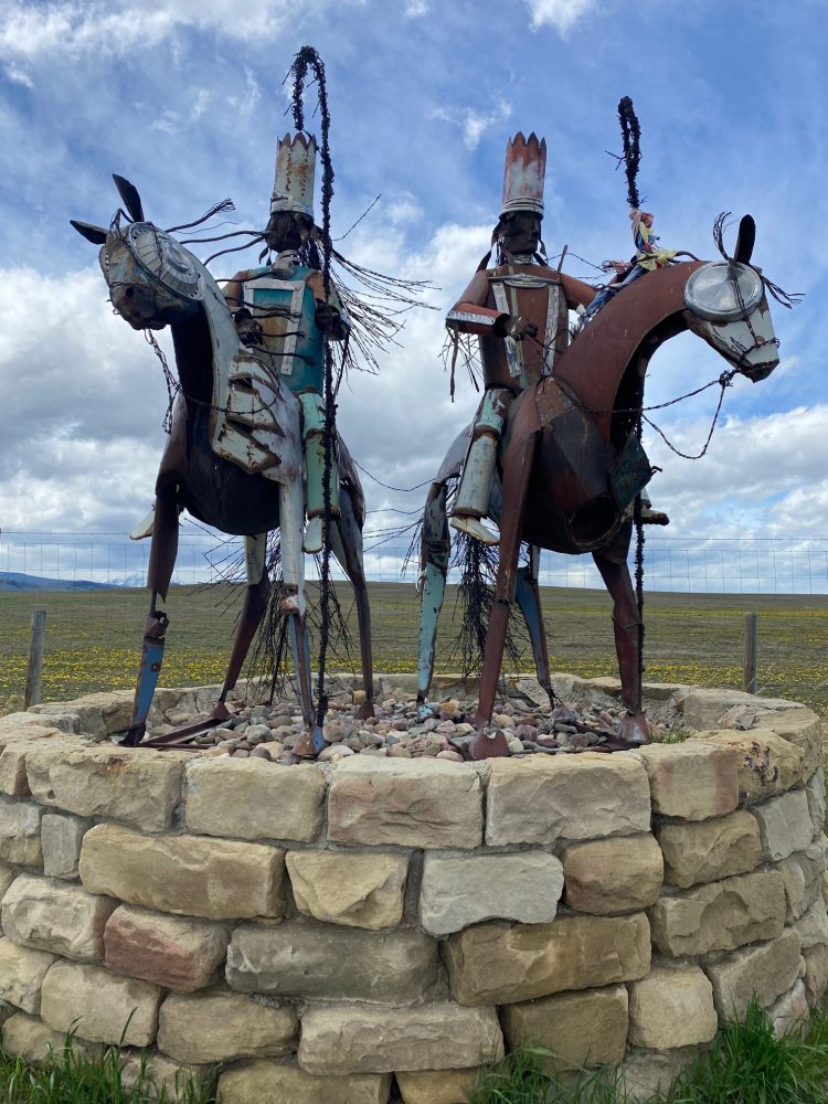 Two metal sculptures of horse riders with crowns, standing on a stone platform under a cloudy sky.