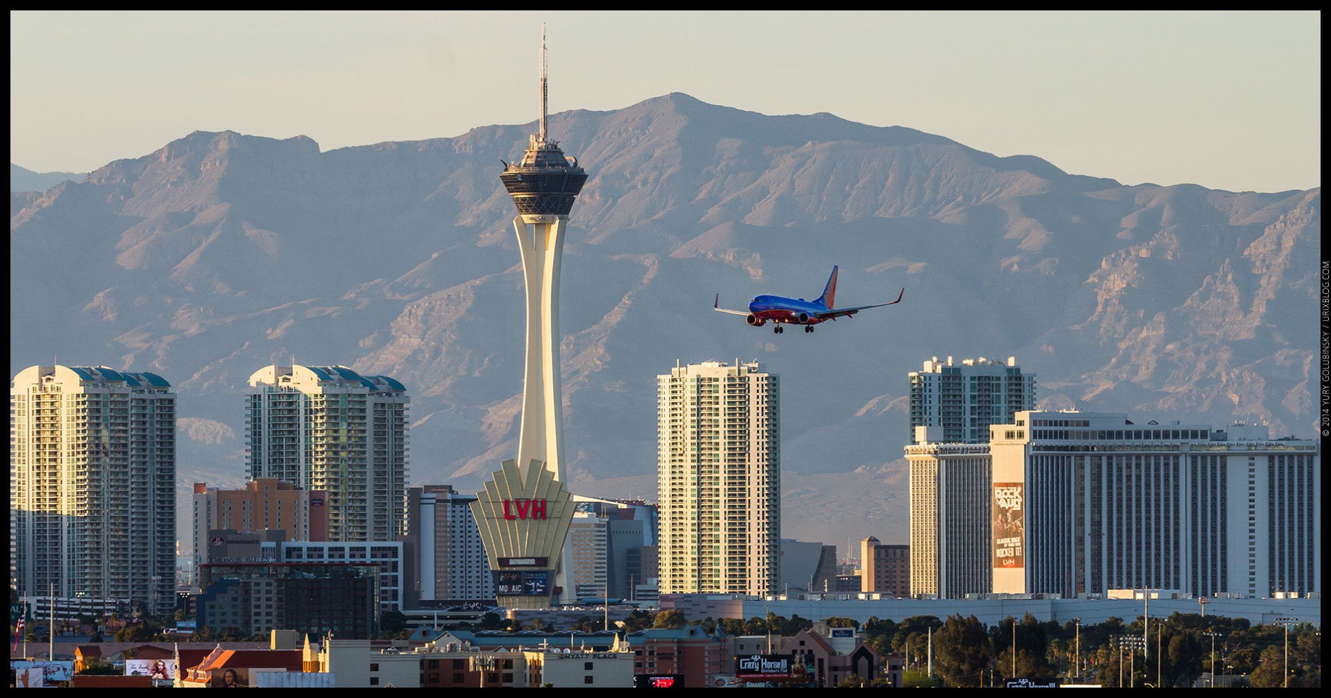 Plane approaching Las Vegas skyline with mountains and tall buildings, including the Stratosphere Tower, in the background.
