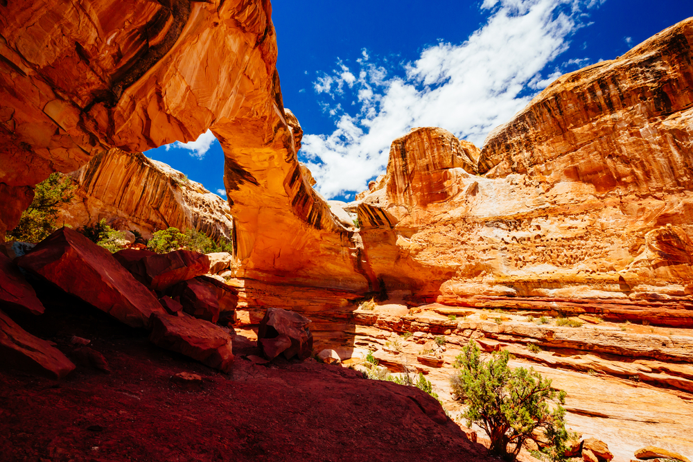 Natural rock arch in a desert landscape with blue sky and scattered clouds.
